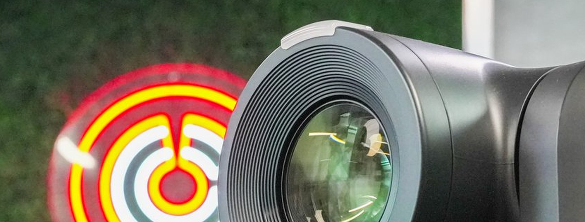 The front element of a PTZ camera, a neon sign thrown out of focus behind it