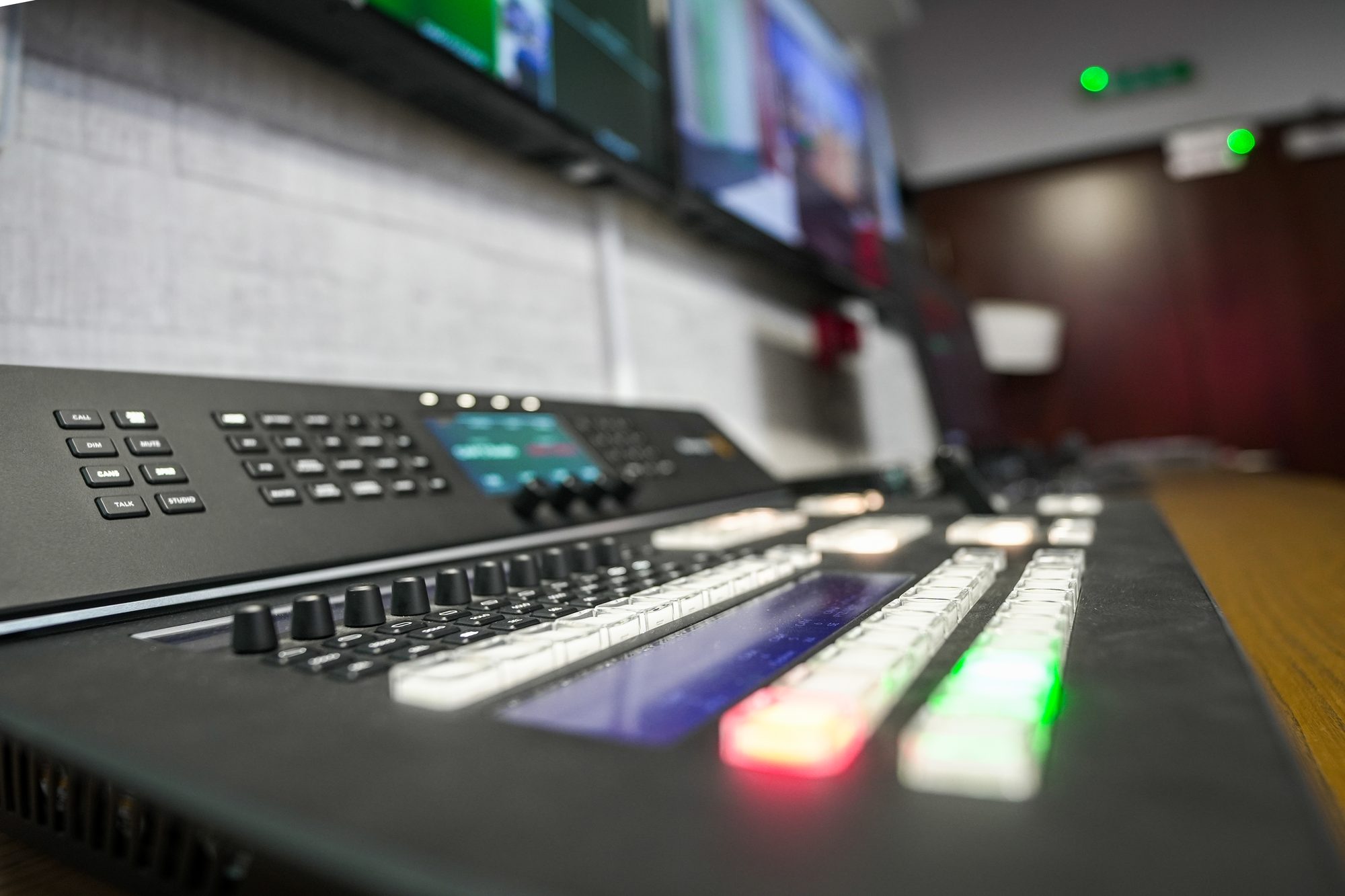 Close on the live production control surface, screens above the desk