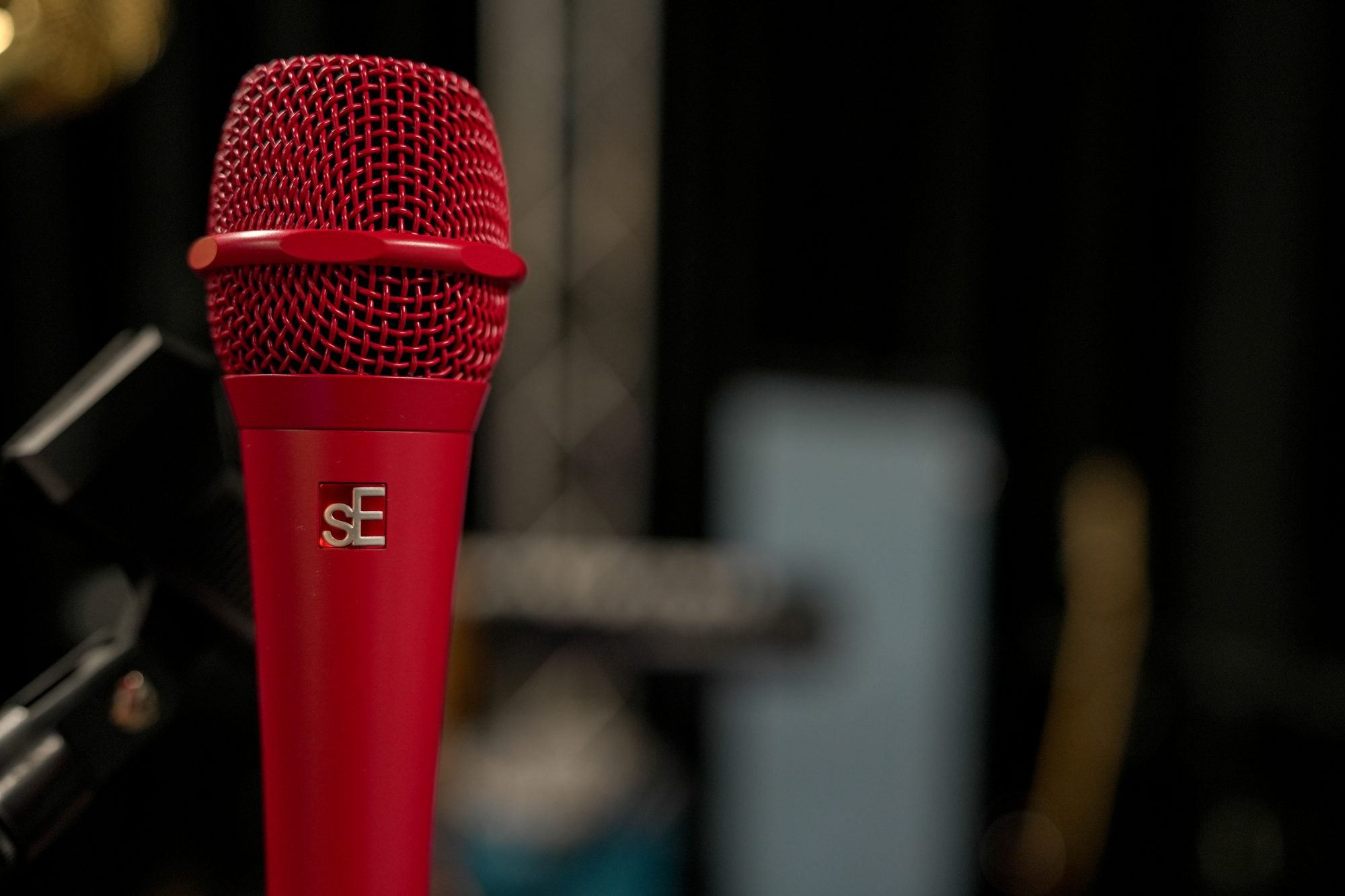 A red sE Electronics stage microphone on its stand, the darkened stage behind it
